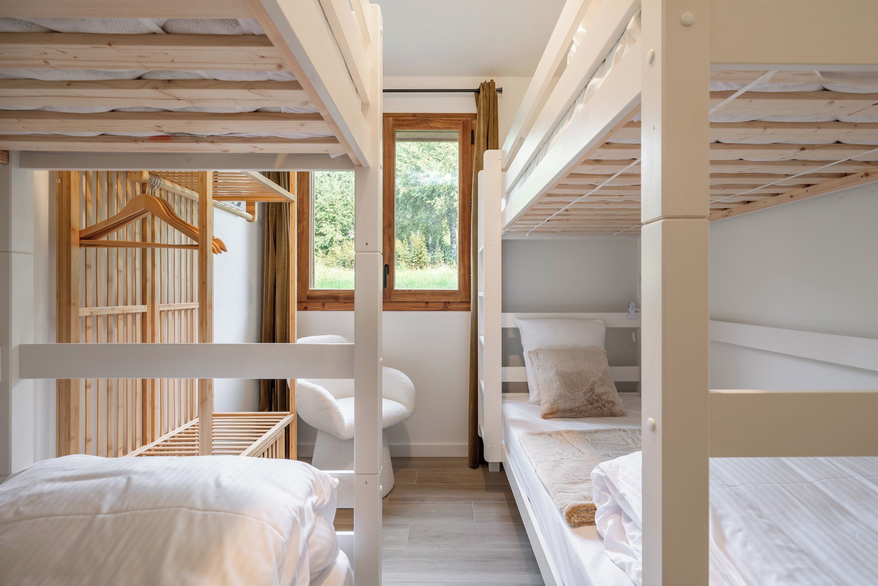 A bunk bed room with a wooden slat ceiling, a small desk, and a window with a view of greenery.