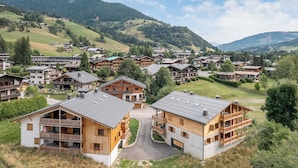 A cluster of wooden buildings with balconies, set in a hilly area with a clear sky.