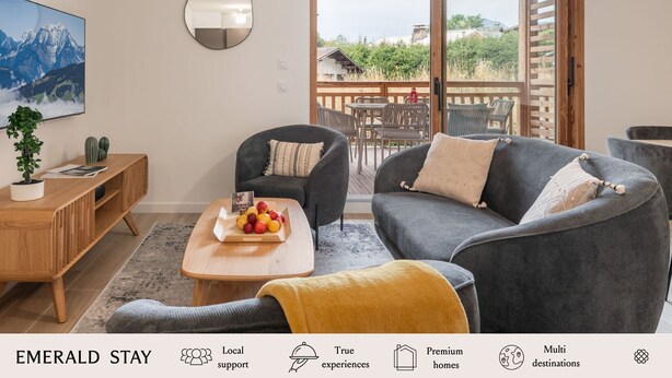 A modern living room with a grey sofa, a wooden coffee table with fruit, a potted plant, and a large painting of mountains.