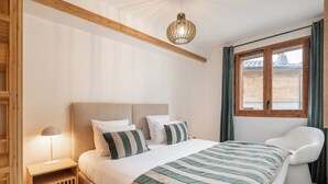 A bedroom with a bed, bedside table, lamp, and a view of the outside through a window.