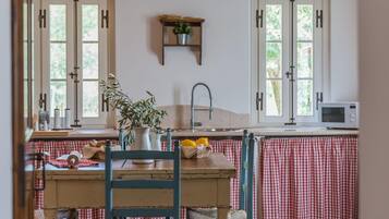 Eine Küche mit zwei Fenstern, einem Spülbecken, einer Mikrowelle und einem Tisch mit Stühlen.