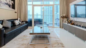 Een moderne woonkamer met een glazen salontafel, een zwarte bank en een groot raam met uitzicht op de stad.