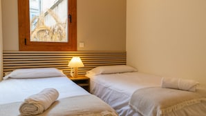 Et hotelværelse med to senge, en træsenggavl, et vindue med udsigt til palmer og en sengetavlelampe.
