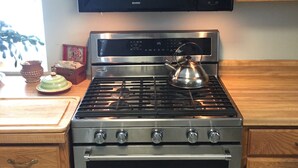 A kitchen with a stainless steel stove, a microwave above it, wooden cabinets, and a window with a view of flowers. - The Bumbletown Hill House (Allouez)