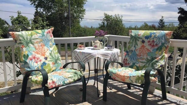 A wooden deck with two chairs and a small table with a teapot and cups. - The Bumbletown Hill House (Allouez)