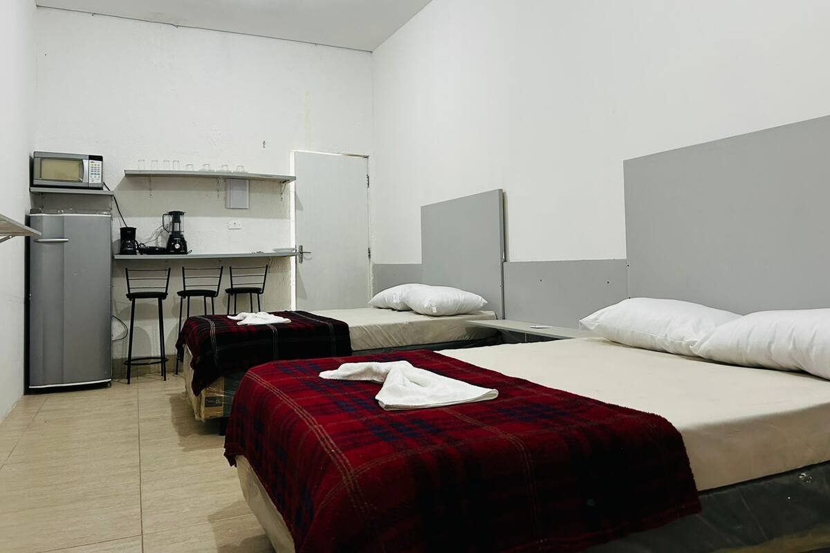 Una habitación pequeña y limpia con una cama, un escritorio con computadora, un microondas y un refrigerador.