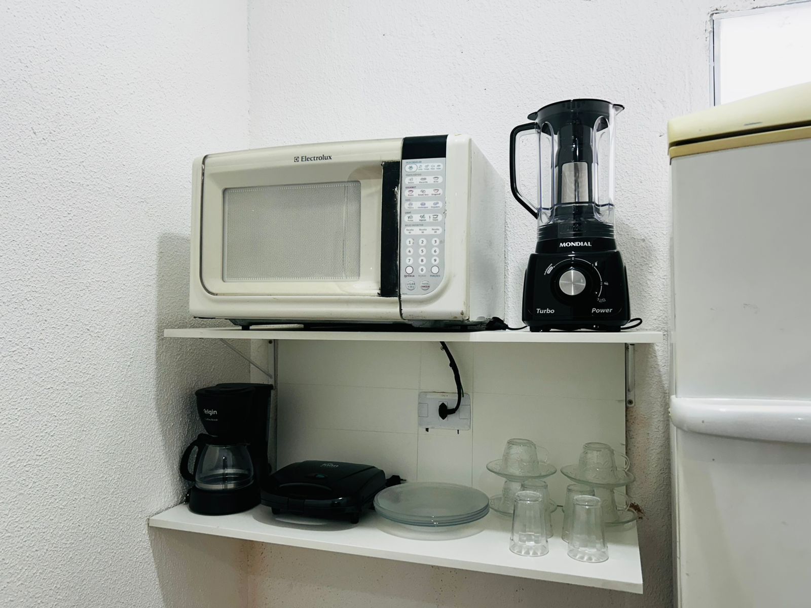 A kitchen with a microwave, a black blender, a coffee maker, and a refrigerator.