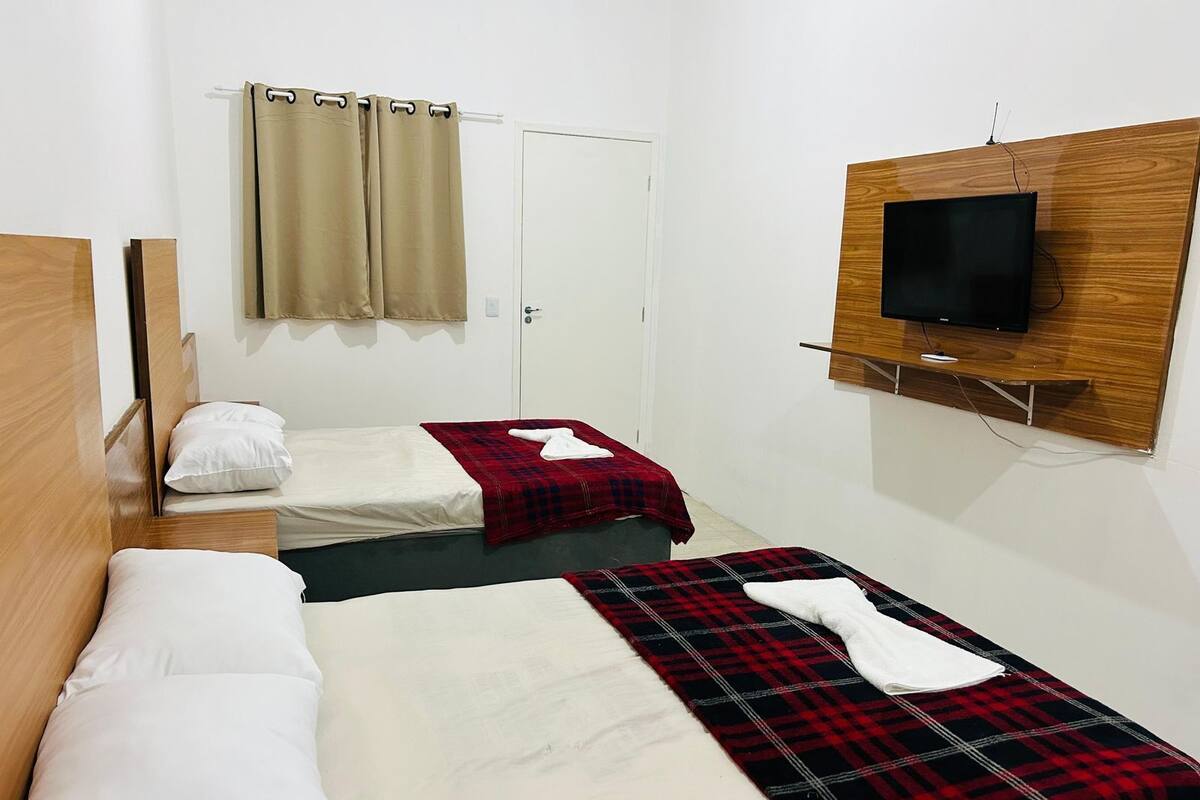 Habitación de hotel con dos camas, un televisor montado en la pared y una puerta con cortina.