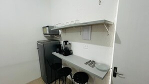 Una kitchenette compacta con microondas, cafetera y taburetes de bar.