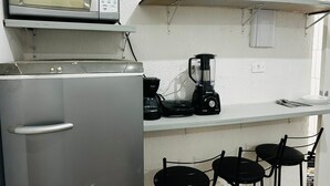 Una kitchenette compacta equipada con microondas, cafetera, licuadora y un refrigerador pequeño.