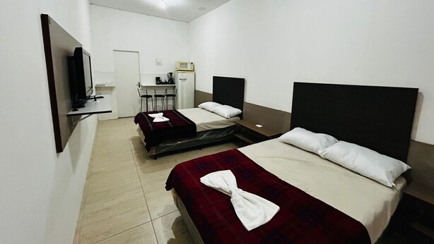 Habitación de hotel con dos camas, un escritorio con silla, televisor y kitchenette.