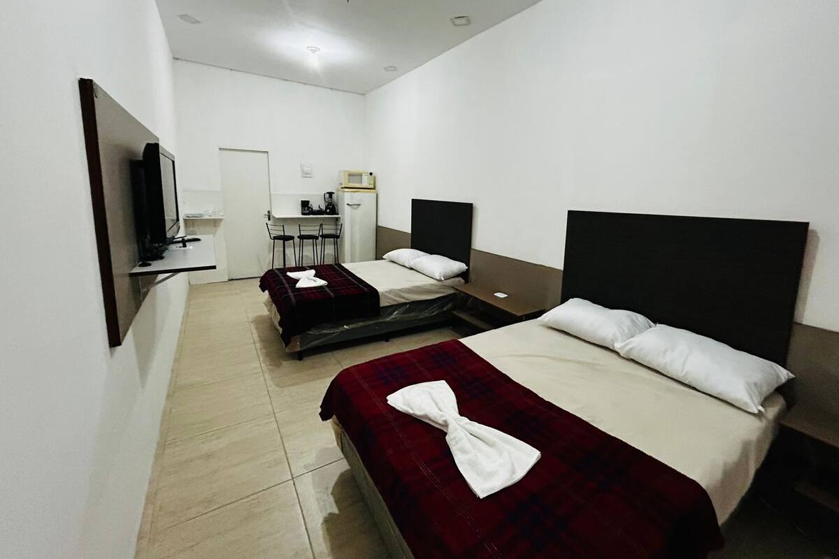 Habitación de hotel con dos camas, un escritorio con silla, televisor y kitchenette.