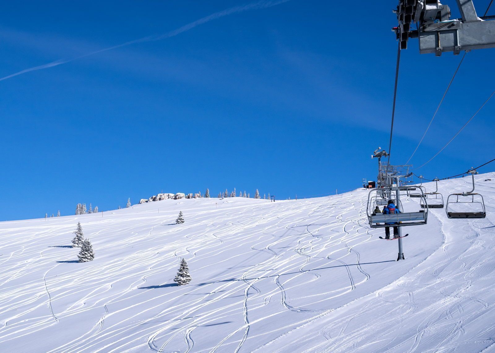Eine Seilbahn auf einem verschneiten Hang mit Skipisten und blauem Himmel.