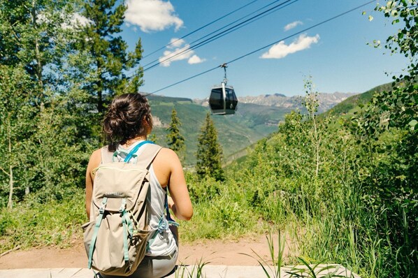 Une personne portant un sac à dos, sur un sentier, avec une télécabine en arrière-plan.
