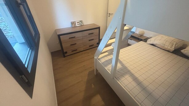 Un dormitorio con una cama litera, un aparador de madera, una mesita de noche y una ventana.
