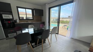 Una cocina moderna con comedor, y un amplio ventanal corredera que da a una zona de piscina.