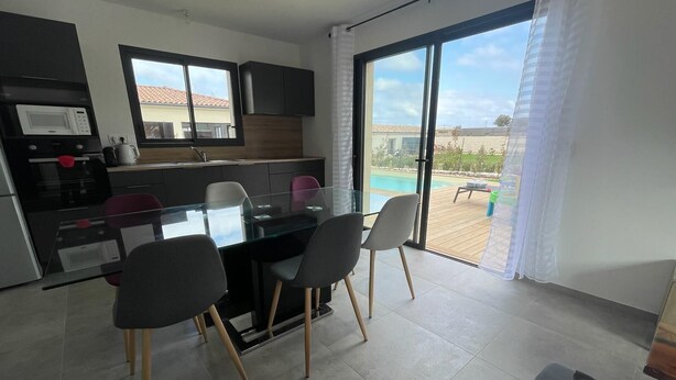 Una cocina moderna con comedor, y un amplio ventanal corredera que da a una zona de piscina.