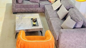 A modern living room with a sectional sofa, a coffee table, and a unique orange pouf. - Midak Mews 2 Oceanview Luxury Apartments (Lekki)