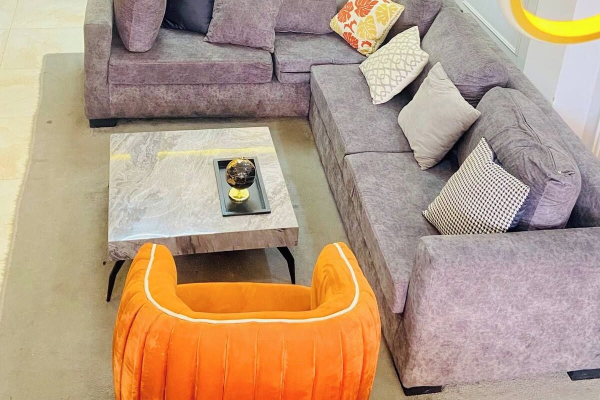 Una sala moderna con un sofá modular, una mesa de centro y un pouf naranja original.