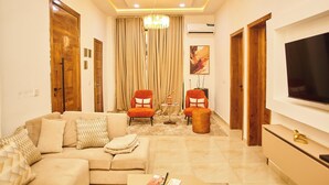 A living room with a sofa, two armchairs, a TV, and a chandelier. - Midak Mews 2 Oceanview Luxury Apartments (Lekki)
