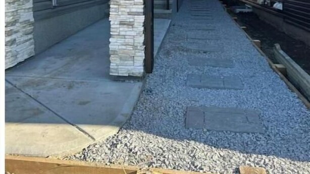 Un bâtiment moderne doté d’un pilier en pierre, d’une allée couverte et d’un chemin de gravier.