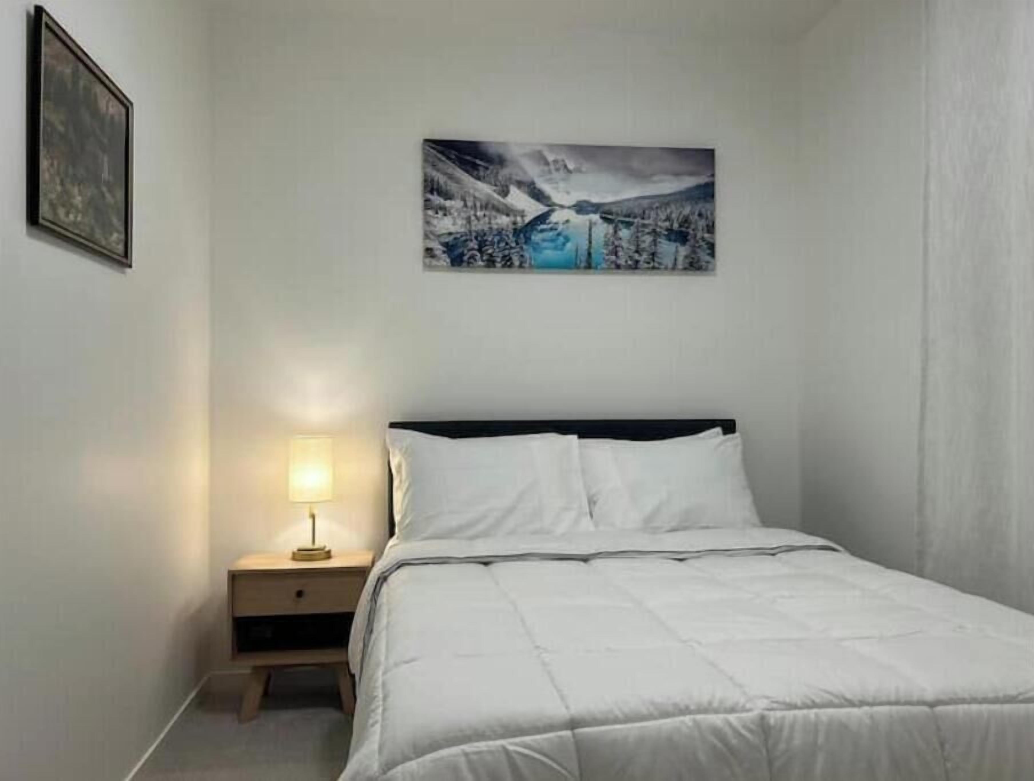 A bedroom with a bed, a nightstand with a lamp, and a framed picture on the wall.