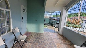 A covered outdoor area with a chair, a door, and a gate leading to a parking area.