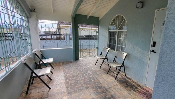 A covered outdoor area with stone flooring, two white chairs, and a large arched window.