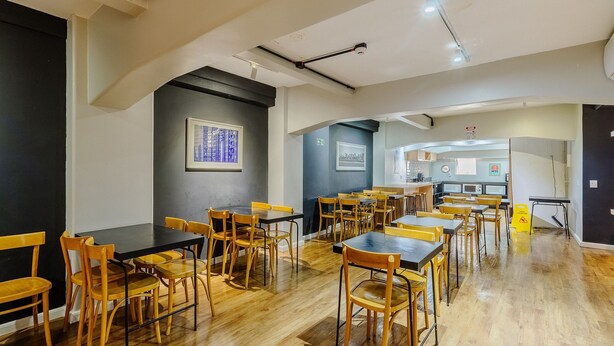 A modern dining area with wooden tables and chairs, a kitchen in the background, and artwork on the walls. - Studio With Prime Location in POA - Els0606 (Porto Alegre)