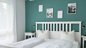 Une chambre avec un lit blanc, des murs de couleur turquoise et des tableaux encadrés accrochés au mur.