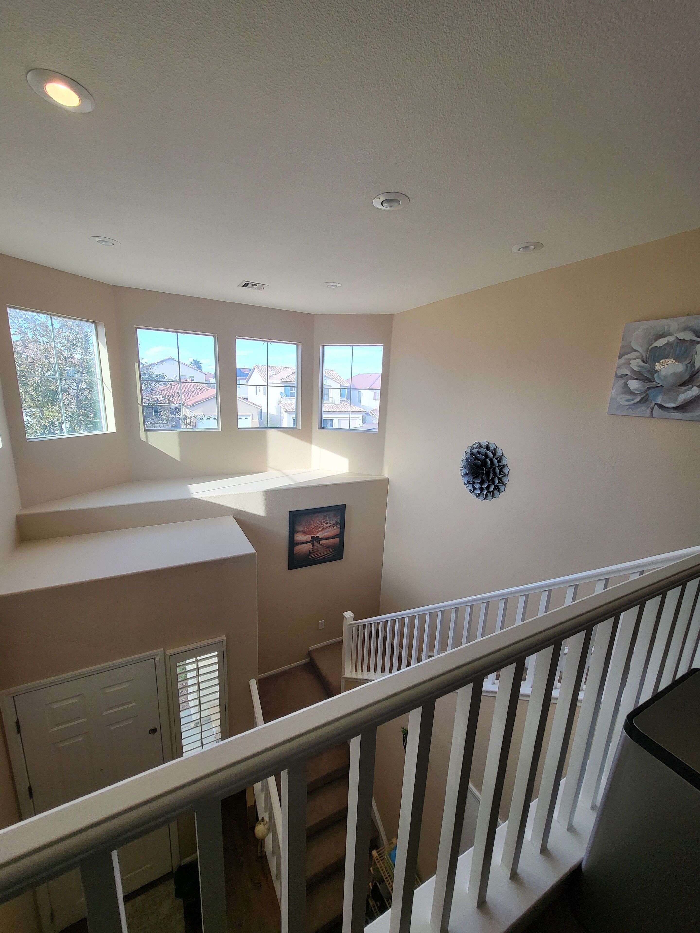 A spacious room with a large window, a framed picture on the wall, and a staircase leading to another level.