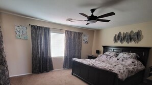 Une chambre avec un grand lit, un ventilateur de plafond et une fenêtre avec des rideaux.