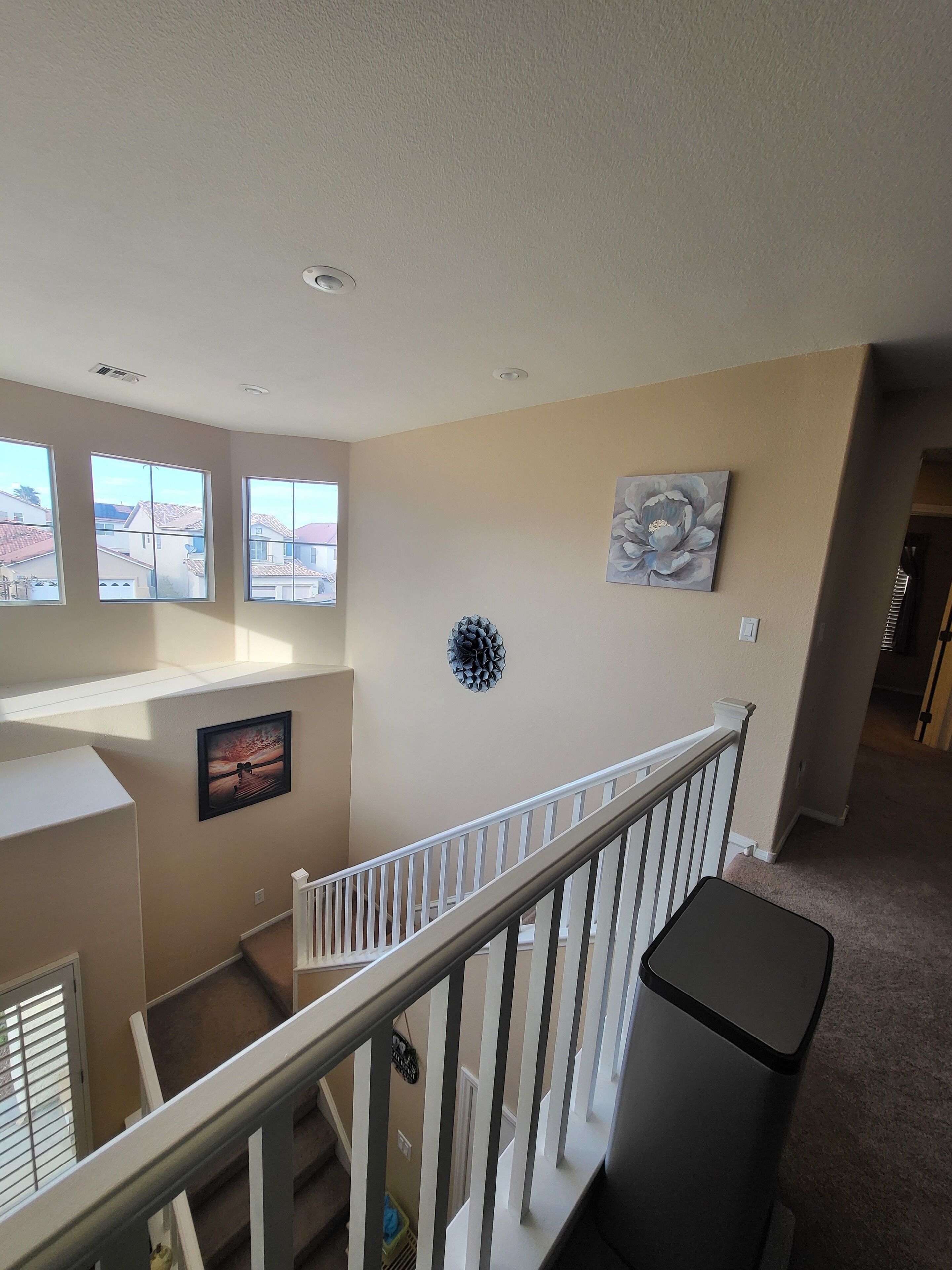 A spacious living area with a high ceiling, large windows, and a staircase with white railings.
