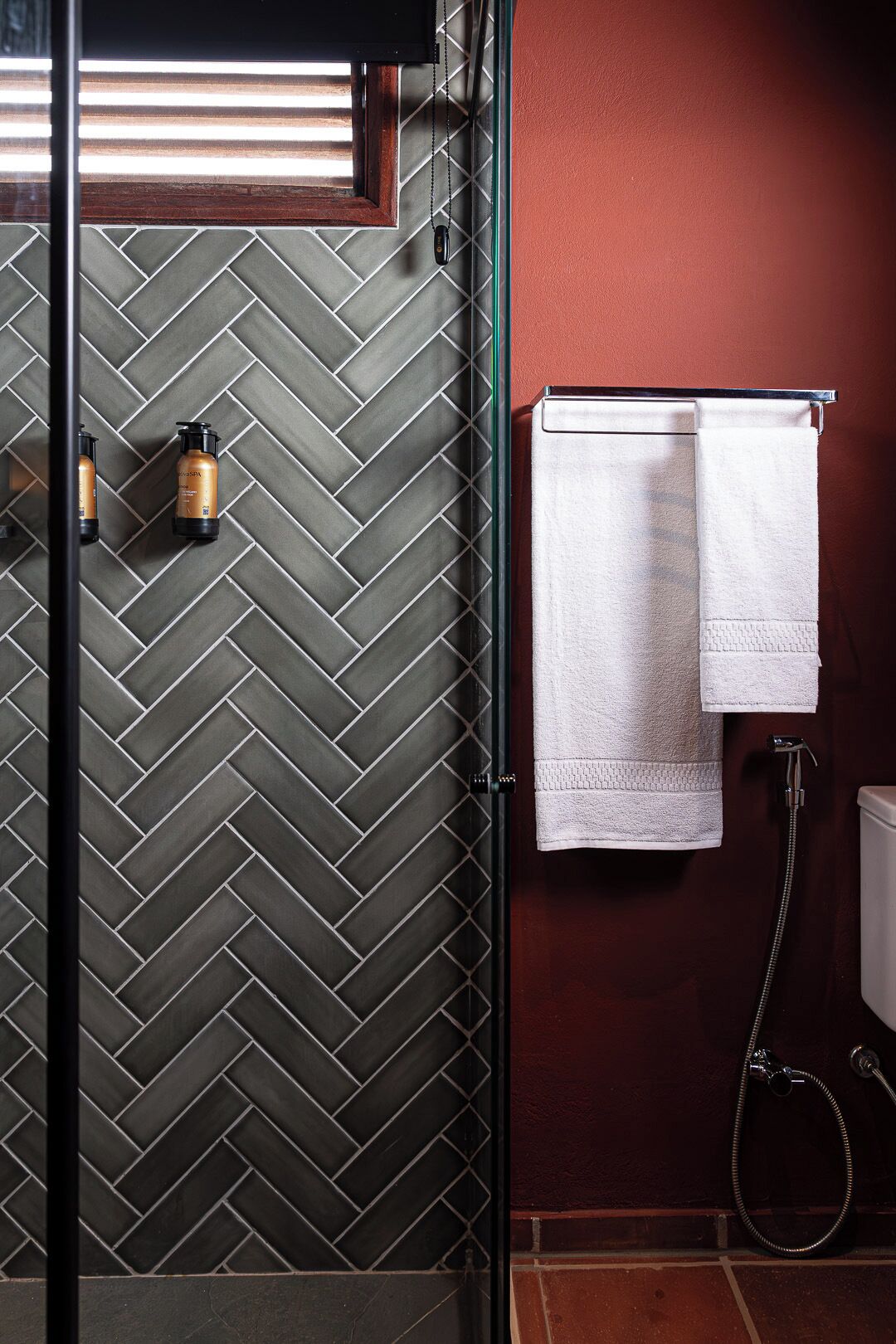 Une salle de bain avec un mur recouvert de carreaux disposés en motif chevron, un porte-serviettes avec deux serviettes blanches et une douche équipée d’un pommeau de douche à main.