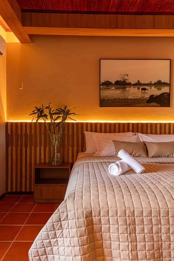 A hotel room with a bed, a bedside table with a vase of plants, and a painting on the wall.