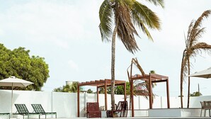 Un espace piscine aménagé avec des chaises longues, une pergola et des palmiers.