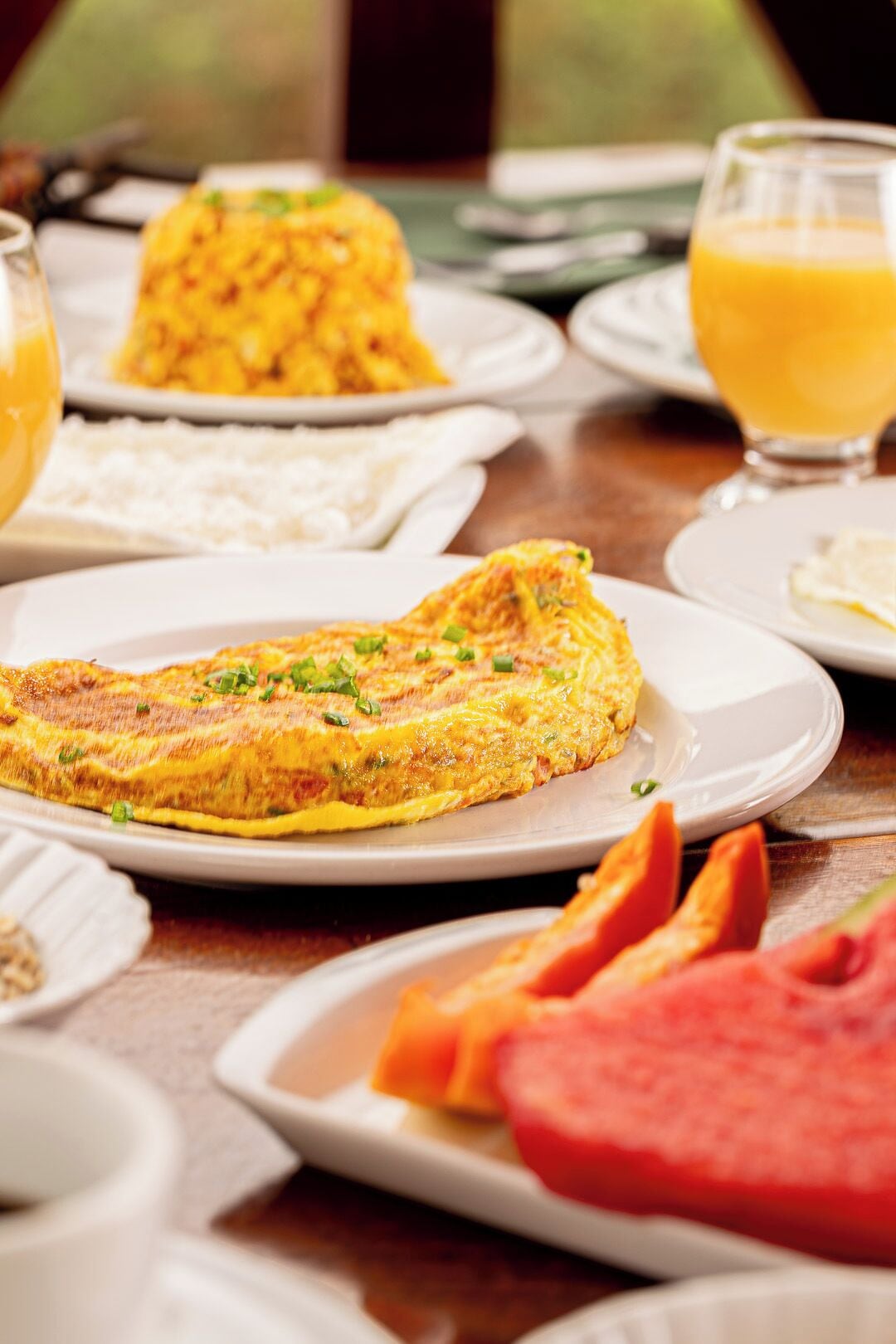 A breakfast setting with a plate of omelette, a bowl of rice, and a glass of orange juice.