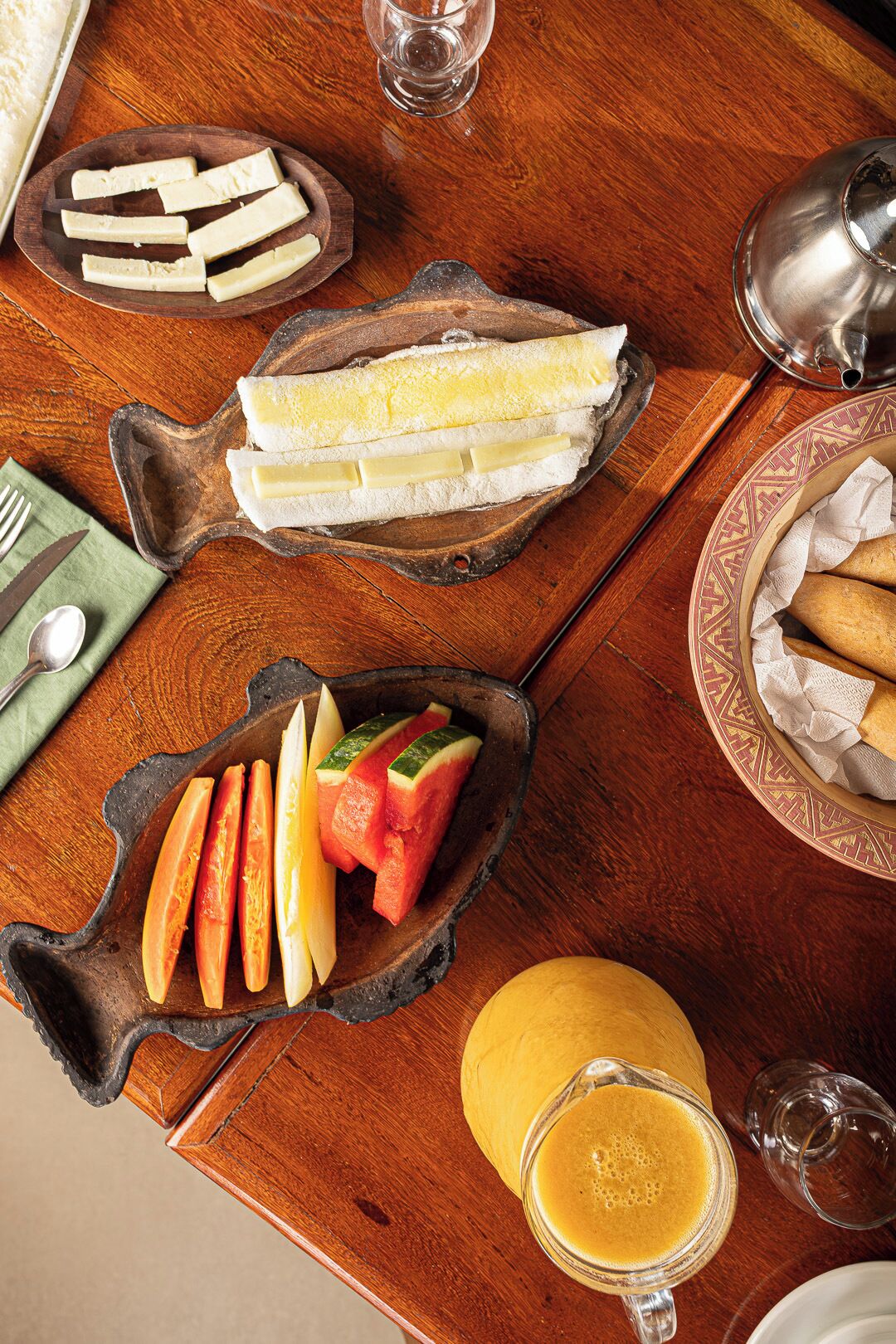 Un desayuno con pan, mantequilla, frutas y un vaso de zumo de naranja sobre una mesa de madera.