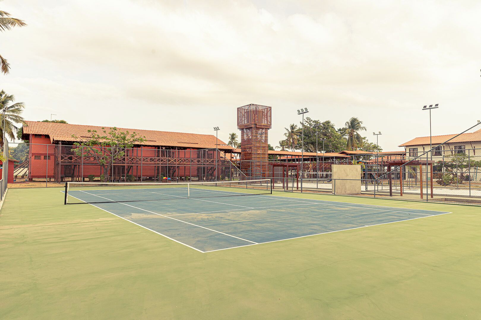 Un court de tennis en plein air, doté d’un filet, entouré d’une clôture et bordé de palmiers.
