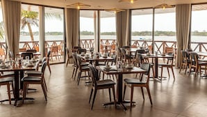 Un restaurant doté de nombreuses tables et chaises, de grandes fenêtres avec des rideaux et de luminaires suspendus.
