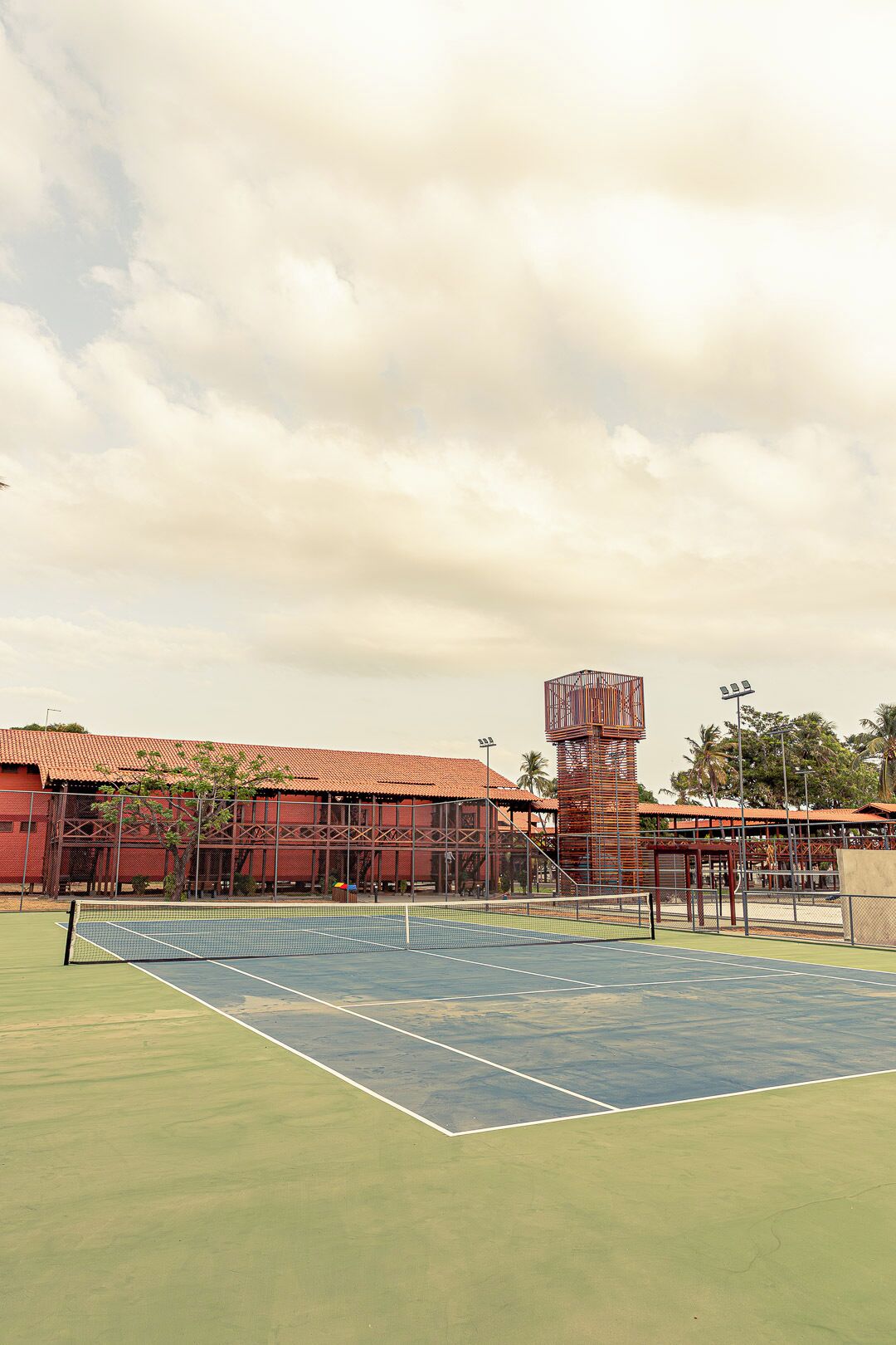 Un court de tennis avec un filet, entouré d’une clôture et bordé d’un bâtiment dont le toit est rouge.