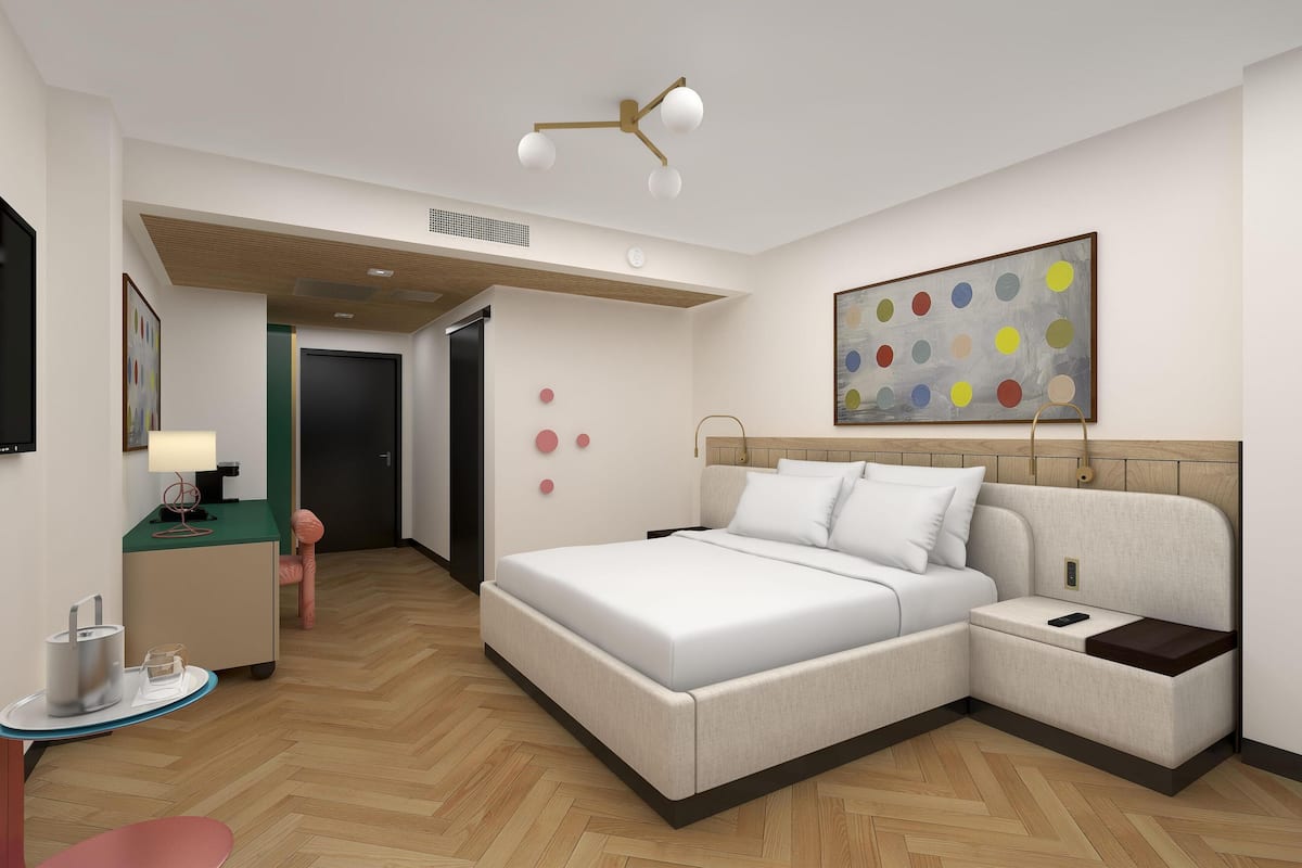 A modern hotel room with a large bed, a desk, a chair, a small table, and a TV.