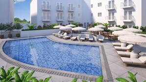 A pool area with lounge chairs and umbrellas, surrounded by a white building with balconies. - Hilton Miami Beach (Miami Beach)