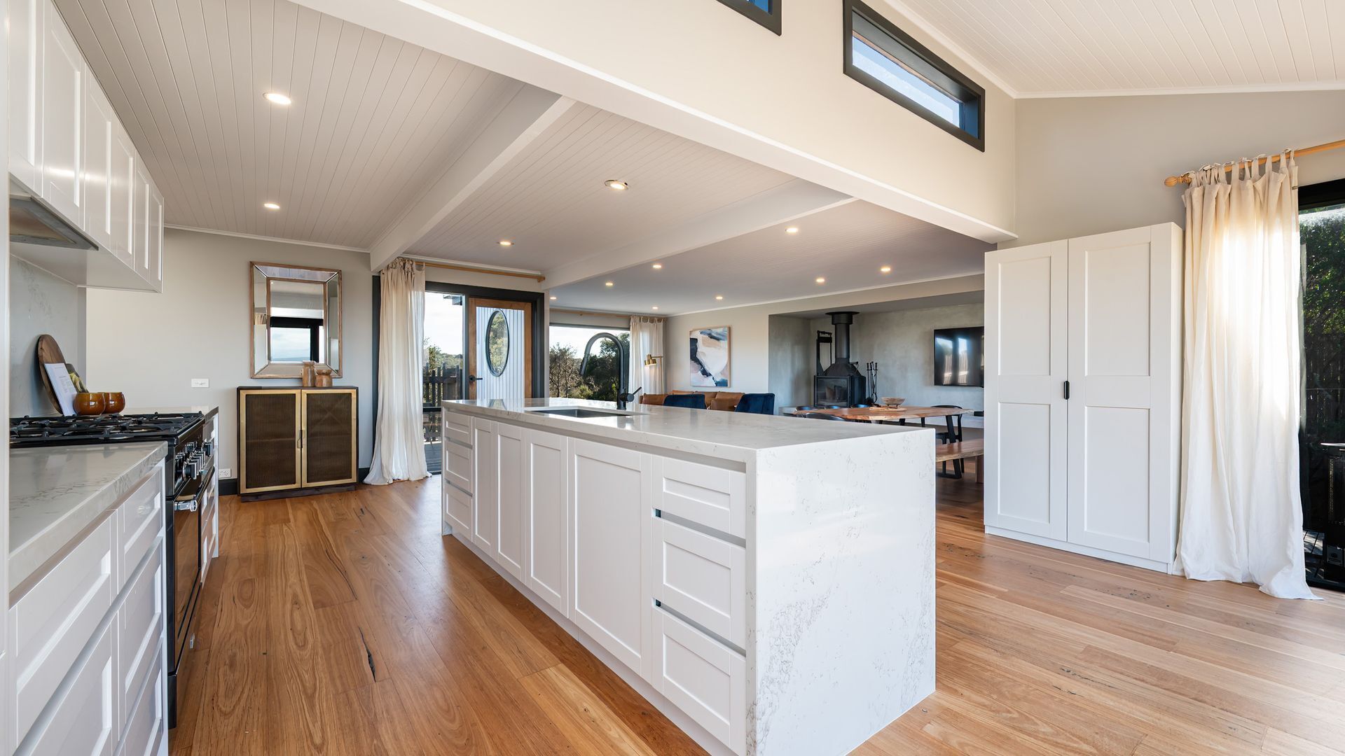 A spacious kitchen with a large island, wooden flooring, and a view of the outdoors.