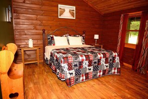 A wooden cabin bedroom with a bed, a nightstand, a chair, a window, and a wooden wall.