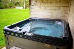 A hot tub with a control panel, set against a wooden wall, outdoors.