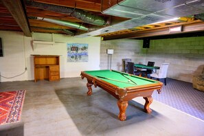 A pool table in a room with a wooden ceiling, a desk, chairs, and a painting on the wall.