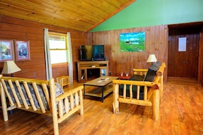 A wooden cabin interior with a TV, wooden furniture, and a painting on the wall.