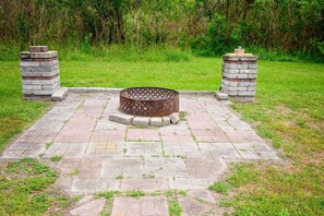 Un foyer circulaire en métal, entouré d’un chemin de briques bordé de pierres.