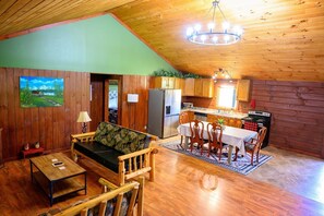 Un intérieur de chalet chaleureux comprenant un coin repas, une cuisine et un salon avec un canapé et une table basse.